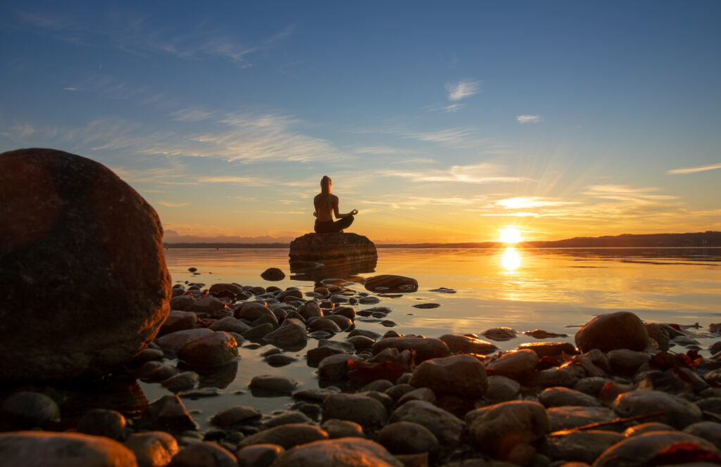 hübsche junge frau macht yoga auf einem stein im wasser see meer im sonnenuntergang abendrot