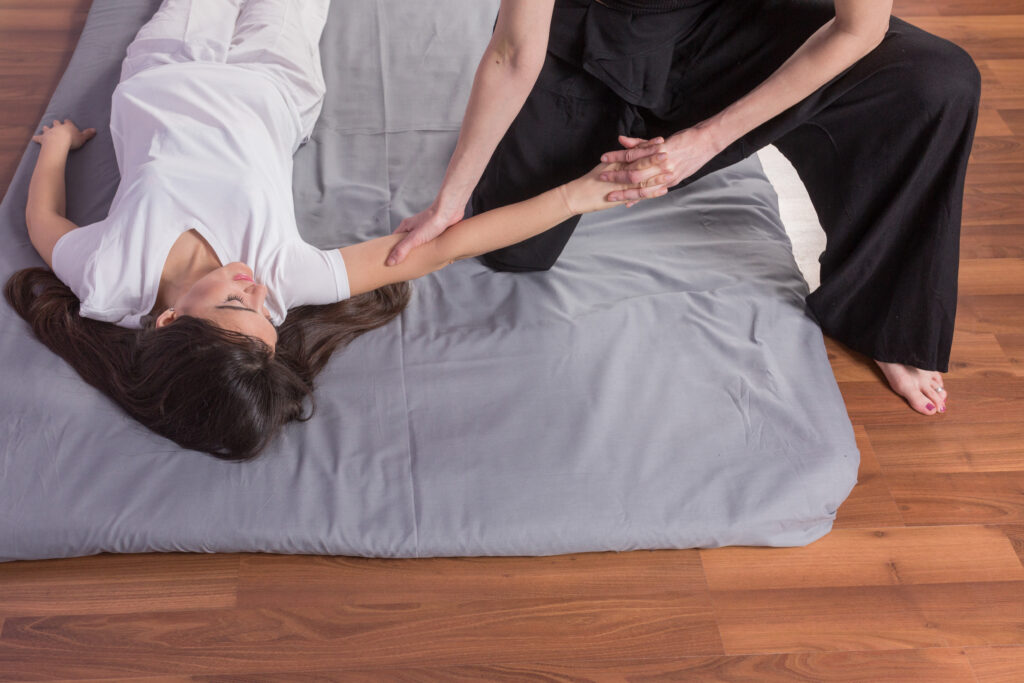 young woman lying while enjoying thai massage by professional wo